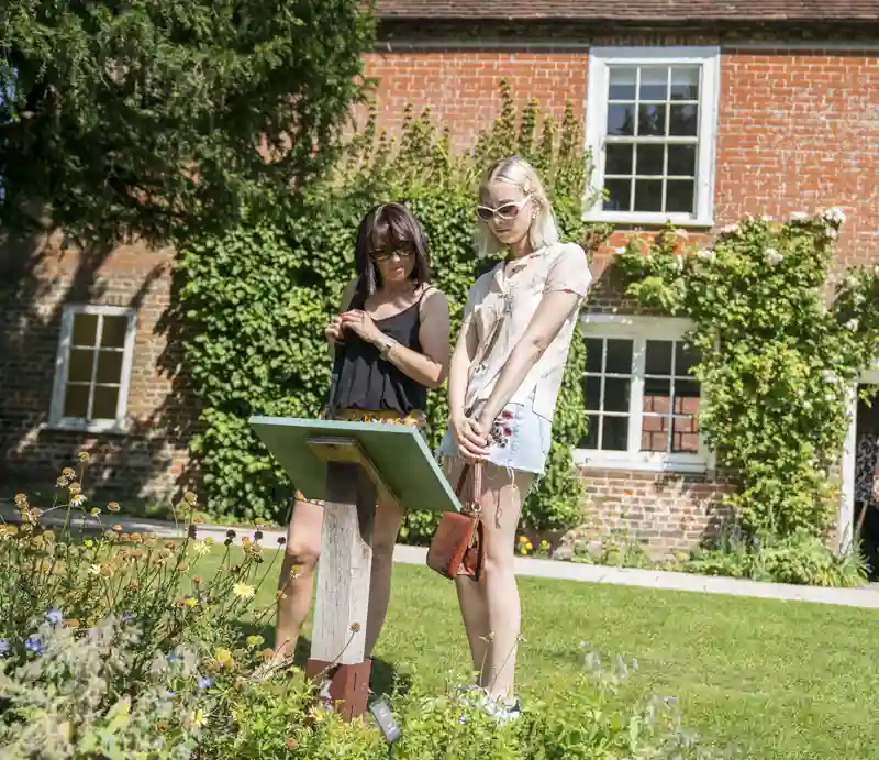 Jane Austen Building exterior with visitors reading an information sign in the garden.