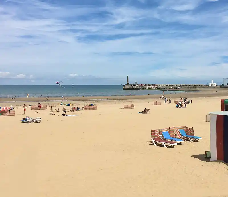 Holiday makers on the sands with promontary and hotels in background.