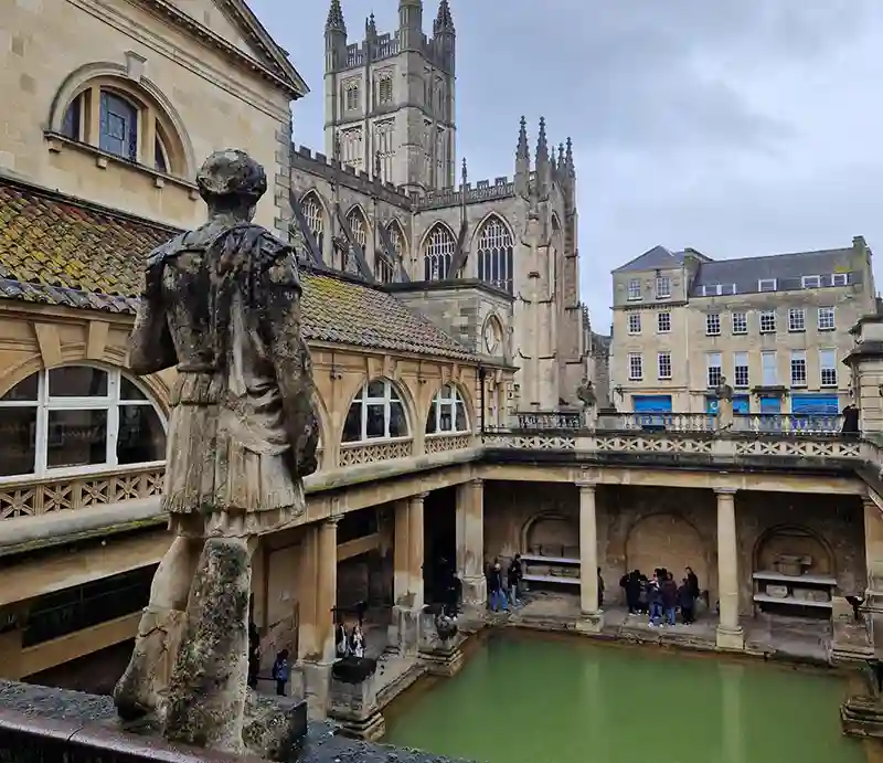Roman Baths Classical architechture with foreground sculptural figure and abbey in background.