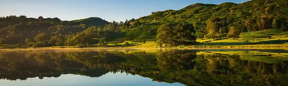 Trees and blue sky reflected in the still lake waters.