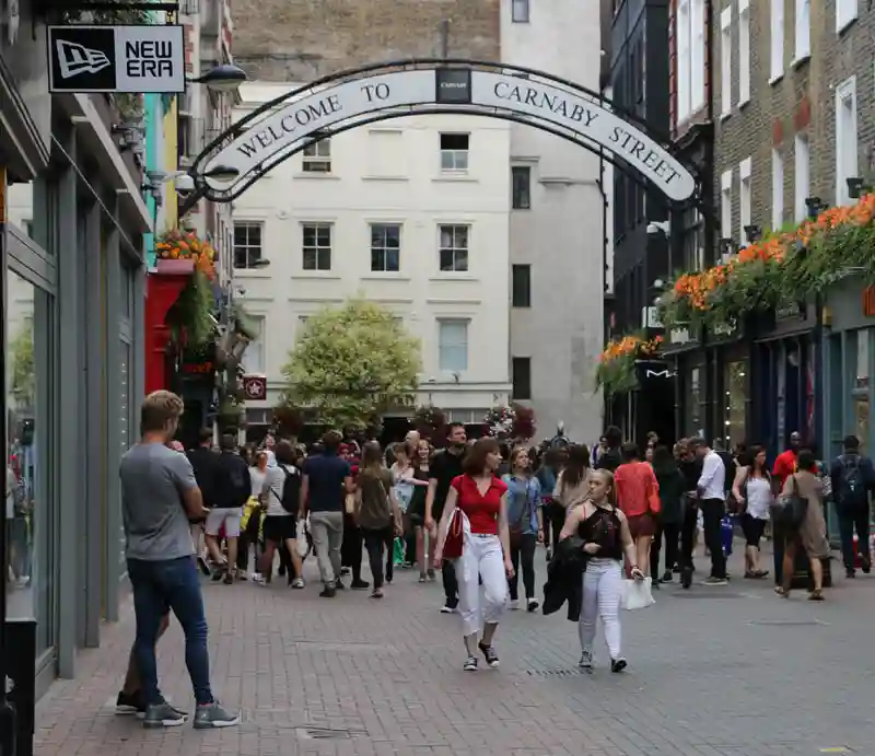 Shoppers with welcome sign at the entrance to Carnaby Street