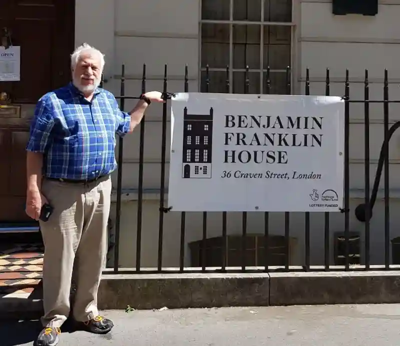 Benjamin Franklin House Guest outside on street next to sign.