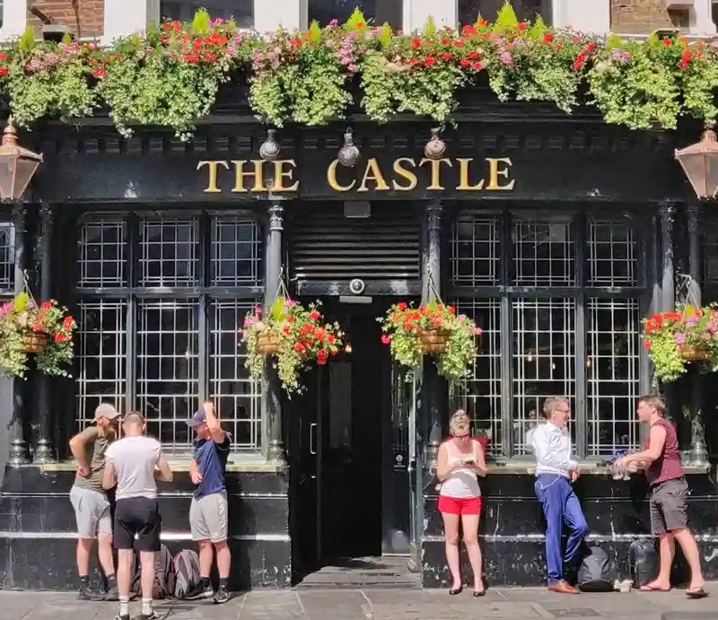 Castle pub Farringdon Customers outside the black-painted exterior with flower arrangements.