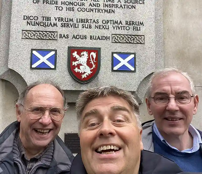 William Wallace Memorial Rob and guests in front of stone plaque with Scottish flags and lion rampant.