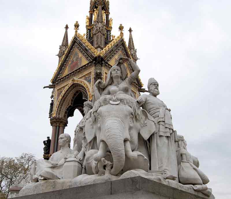 The Gothic style tower behind stone sculpted figures.