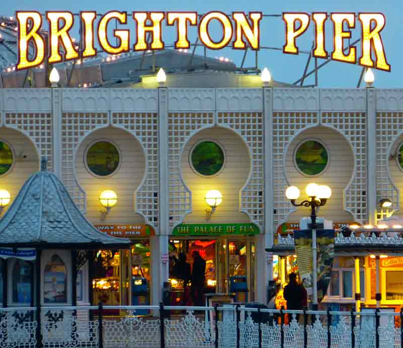 Brighton Palace Pier Neon sign above Victorian railings and wooden structure.