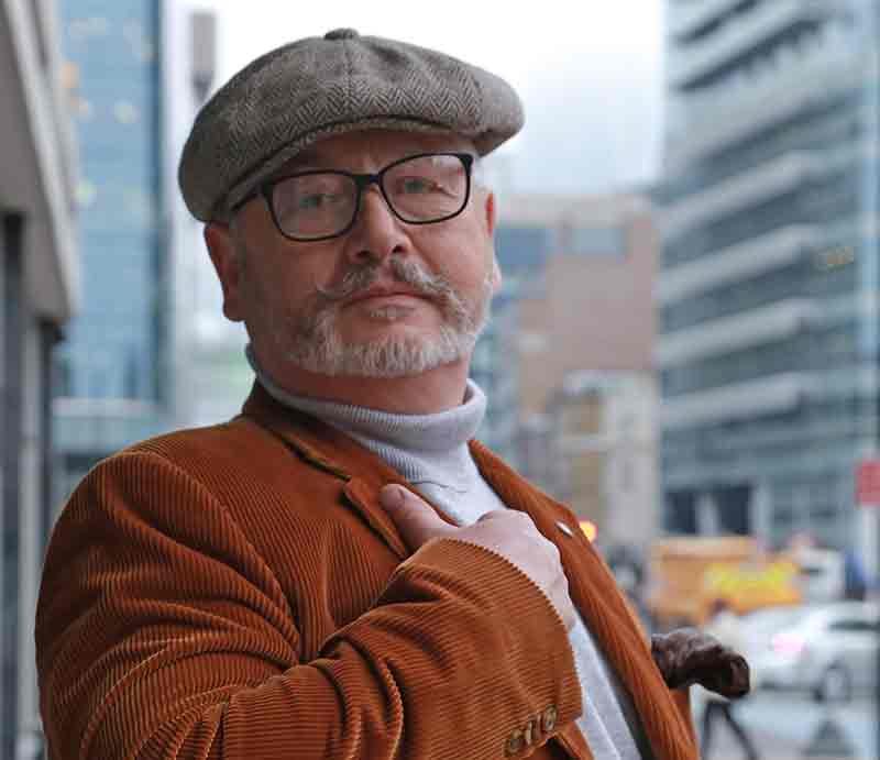 Lee Cooper Tour Guide With flat cap and brown corduroy jacket, modern City offices behind.