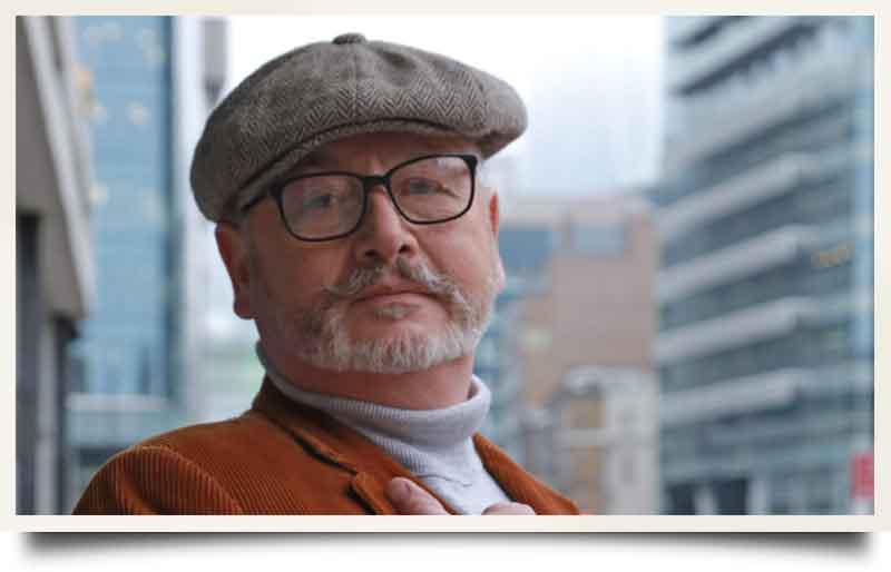 Lee Cooper With flat cap and brown corduroy jacket, modern City offices behind.