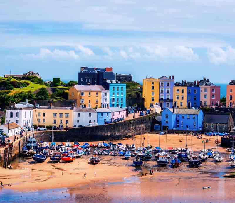 Wales Tour Tenby Harbour at low tide with fishing boats and brightly painted cottages.